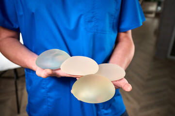 Close-up of female plastic surgeon demonstrates breast implants to a patient for her new breast. The plastic surgeon holds breast silicone implants. Breast augmentation concept. Breast Implant Samples