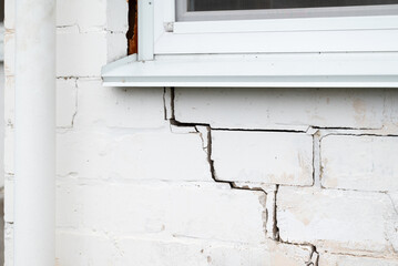 Cracked brick wall of private house. Crack under the window on white brick wall, problems with foundation