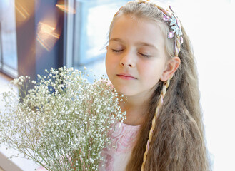 Cute girl closing her eyes, close-up, Caucasian man with blond hair and a pink pastel dress with a bouquet of gypsophila flowers. Fragrance Spring concept