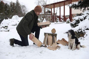 Man chopping wood with axe next to cute dog outdoors on winter day