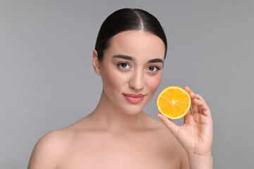 Beautiful young woman with piece of orange on grey background
