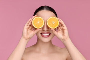 Beautiful young woman covering face with pieces of orange on pink background
