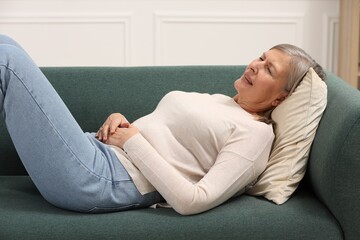Menopause. Woman suffering from abdominal pain on sofa at home