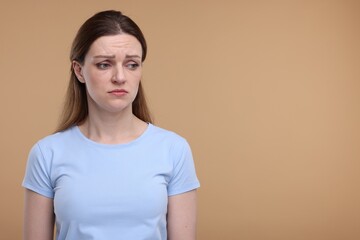 Portrait of sad woman on beige background, space for text
