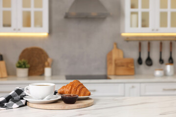 Breakfast served in kitchen. Fresh croissant, coffee, and jam on white table. Space for text
