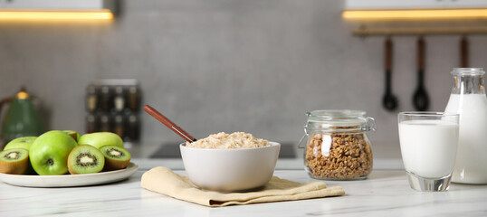 Breakfast time. Tasty oatmeal in bowl, fruits, granola and milk on white marble table. Banner design