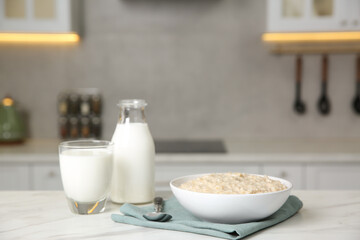 Breakfast time. Tasty oatmeal in bowl and milk on white marble table. Space for text