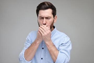 Sick man coughing on light grey background. Cold symptoms