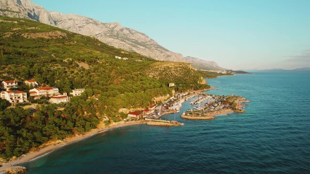 Coast of Makarska Riviera in Croatia. Harbor at the foot of Biokovo mountains. Warm glow of the evening sun with azure waters of the Adriatic Sea.