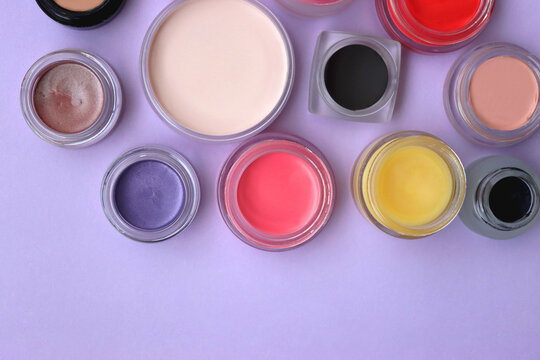 Bowls with various colorful cream beauty products on purple background. Top view.