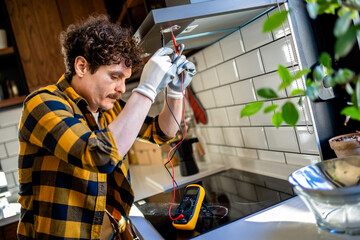 Fototapeta na wymiar Latino man fixing aspirator in the kitchen with multimeter.