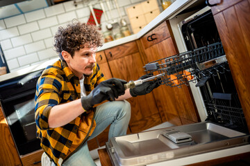 Latino man fixing dishwasher in the kitchen.