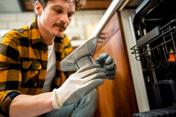 Latino man fixing dishwasher in the kitchen.