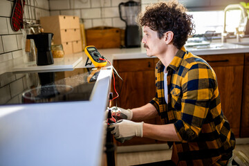 Latino man using multimeter for fixing stove. - obrazy, fototapety, plakaty