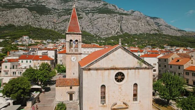Old church in Makarska from above. Historic cathedral overlooks the town. Aerial view of red-roofed city with Biokovo mountain.