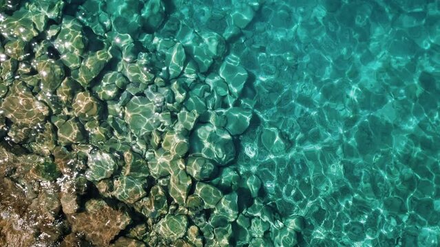 Clear Adriatic sea waters. Pristine ocean waters shimmer in the sunlight, revealing a textured sea bed, aerial top down circle view.