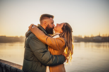 Fototapeta premium Happy couple enjoy spending time together outdoor on a sunset. Man is kissing his woman in chin.