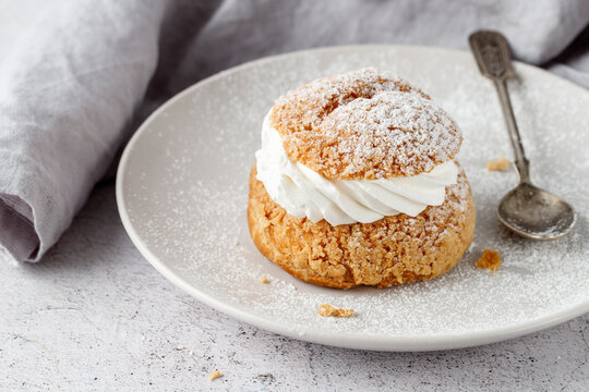 Cream puffs, semla, pastry from choux covered sugar powder on white plate over stone table background. Sweet dessert with chantilly cream