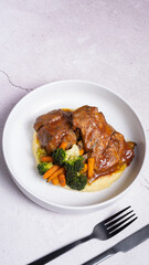 A plate of beef ribs in red sauce with vegetables and mashed potatoes with black cutlery