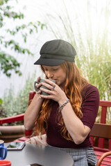 Vertical portrait with pensive young redhead woman drinking latte at coffee bar garden - Focus on face