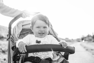 Happy laughing baby girl enjoying a walk in countryside sitting in the modern stroller - Sweet...