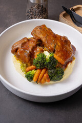 Close-up plate of beef ribs in barbecue sauce with vegetables and mashed potatoes on dark background