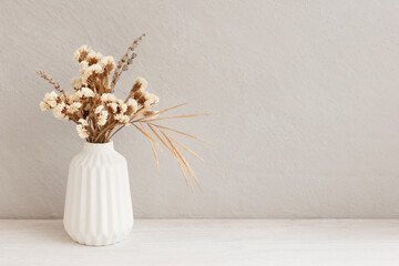 Minimalistic composition of dried flowers in white vase on gray vintage textured wall background and on wooden shelf. Front view, mock up, copy space