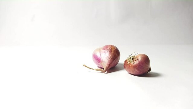 A whole red onion rolls from the right of the frame on a plain white background