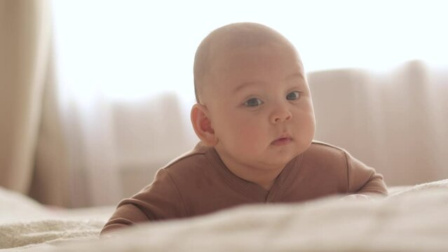 The baby lies on his stomach and looks thoughtfully slow motion close-up