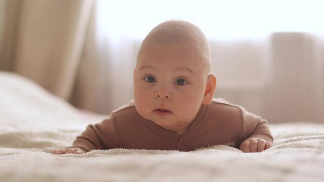 the baby boy looks at the camera and laughs close-up the newborn is lying on his tummy at home on the bed