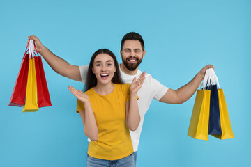 Excited couple with shopping bags on light blue background