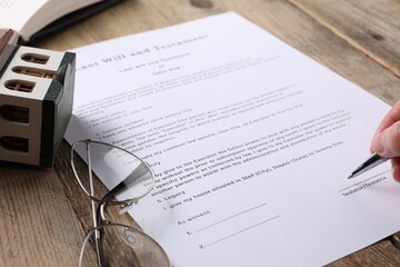 Woman signing Last Will and Testament at wooden table, closeup - obrazy, fototapety, plakaty