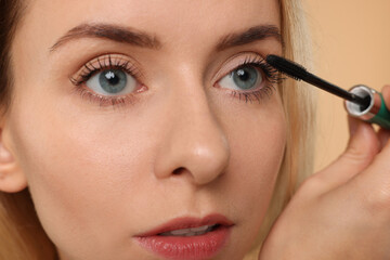 Beautiful woman applying mascara on beige background, closeup