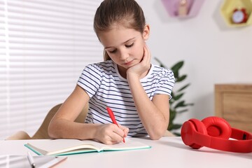 E-learning. Cute girl taking notes while studying online at table indoors