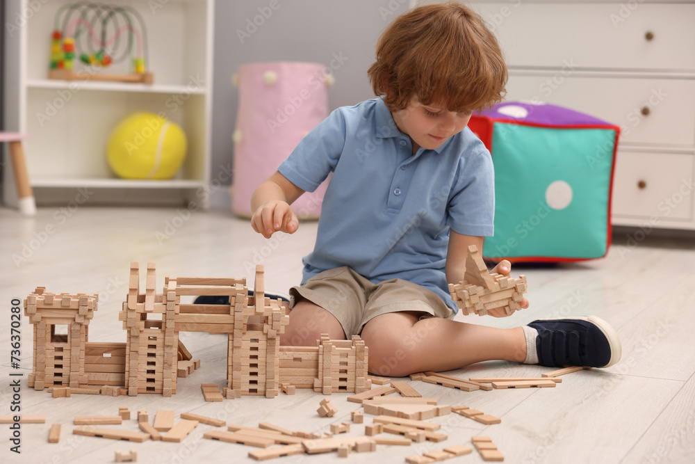 Wall mural Little boy playing with wooden construction set on floor in room. Child's toy