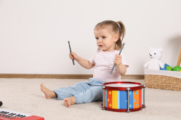 Cute little girl playing with drum and drumsticks at home