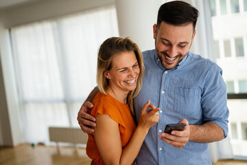 Smiling couple embracing while using a smartphone. People sharing social media on mobile phone.