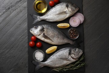 Fresh raw dorado fish, lemon wedges, spices and tomatoes on black table, flat lay