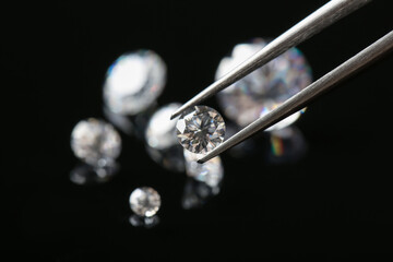 Tweezers with beautiful shiny diamond against black background, closeup