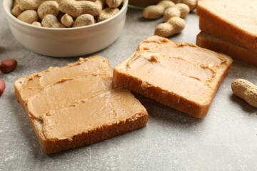 Tasty peanut butter sandwiches and peanuts on gray table, closeup