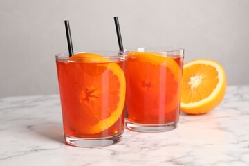 Aperol spritz cocktail, orange slices and straws in glasses on white marble table