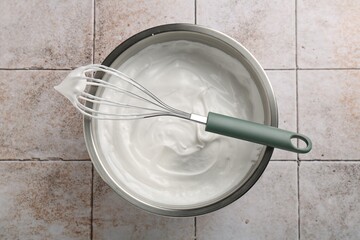Bowl and whisk with whipped cream on tiled table, top view