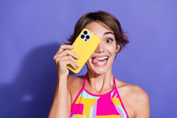 Photo of young lady in pink singlet crazy face hide eye photographer amateur using smartphone tongue out isolated on purple color background