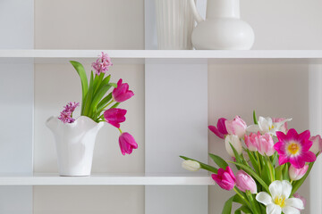 white and pink tulips in vases on white shelf