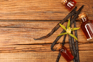 Aromatic vanilla extract, pods and flower on wooden table, flat lay. Space for text