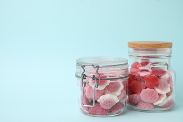 Tasty pink candies in glass jars on light blue background, space for text