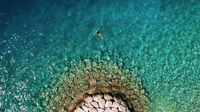 Swimmer in crystal clear waters. A lone woman in swimwear floats above the rocky seabed, basking in the sun's embrace.