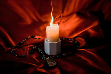 burning candle, a symbol of the moon, an amulet lying on a red natural background. pagan wiccan,...