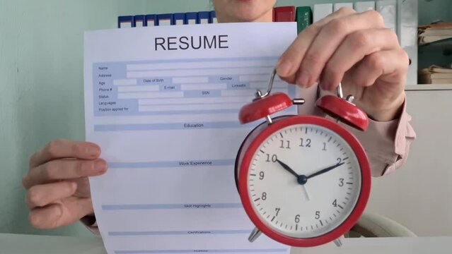 Closeup of hands holding red alarm clock and resume with focus on time management, deadline, and recruitment concept