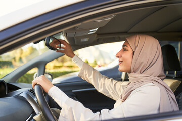 beautiful young Muslim woman in veil adjusts car rearview mirror to start driving